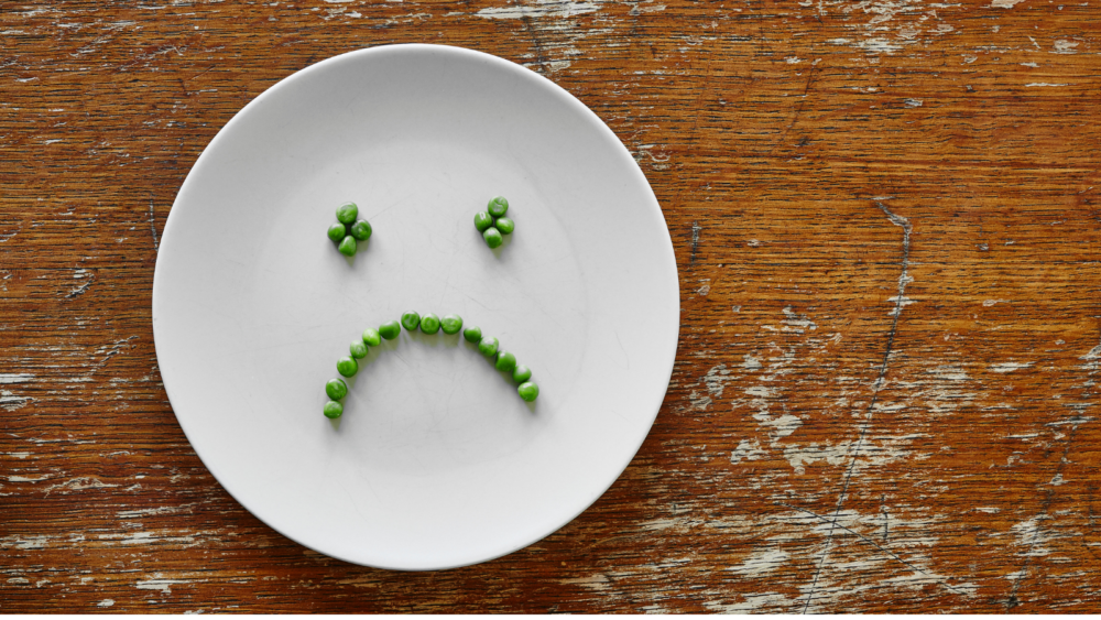 栄養不足をイメージする空っぽの皿とわずかな大豆の写真